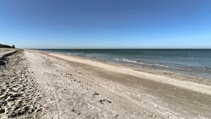 Uma praia com extensa faixa de areia e águas calmas.