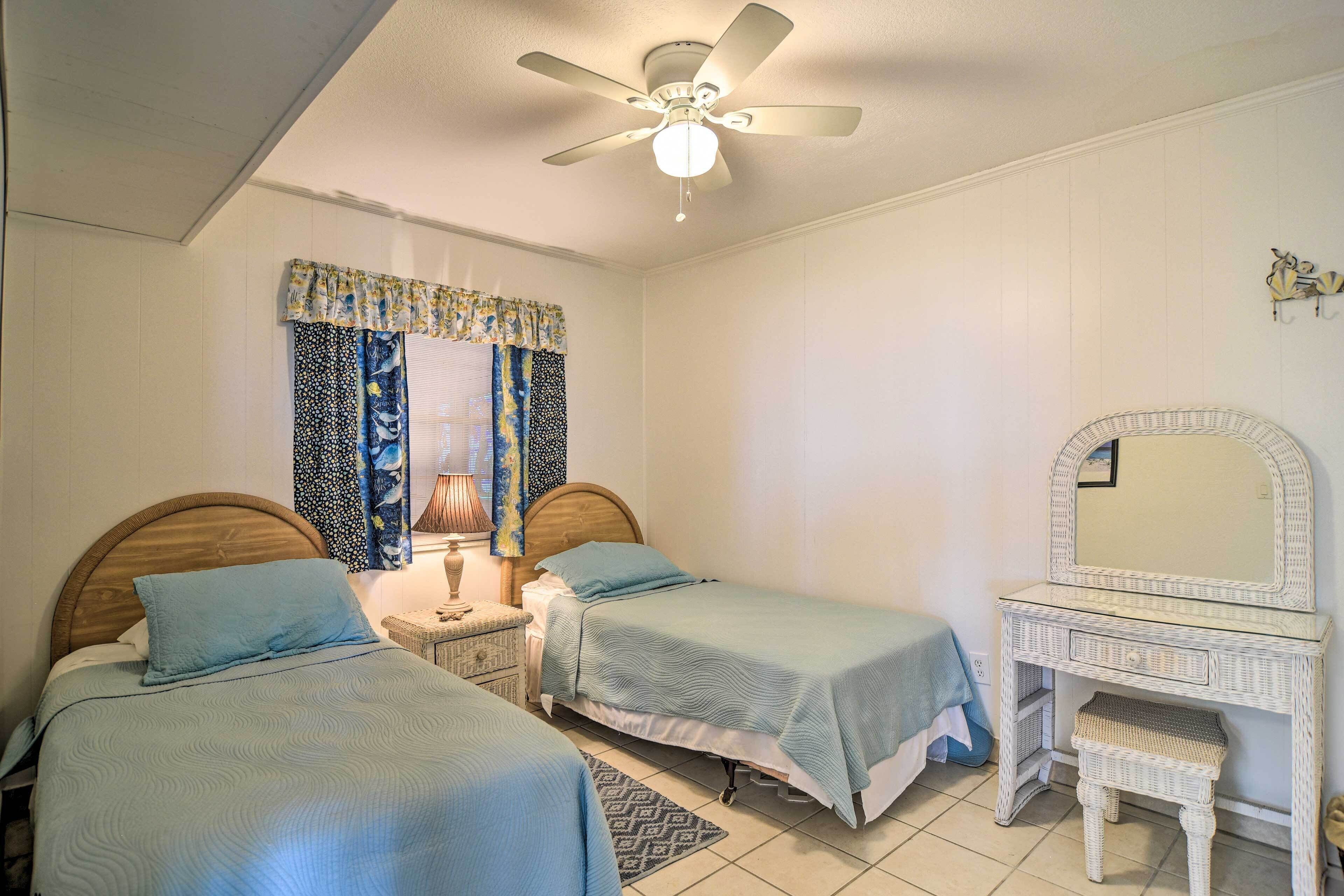 A bedroom with two single beds, a nightstand, a dresser, a ceiling fan, and a window with patterned curtains.