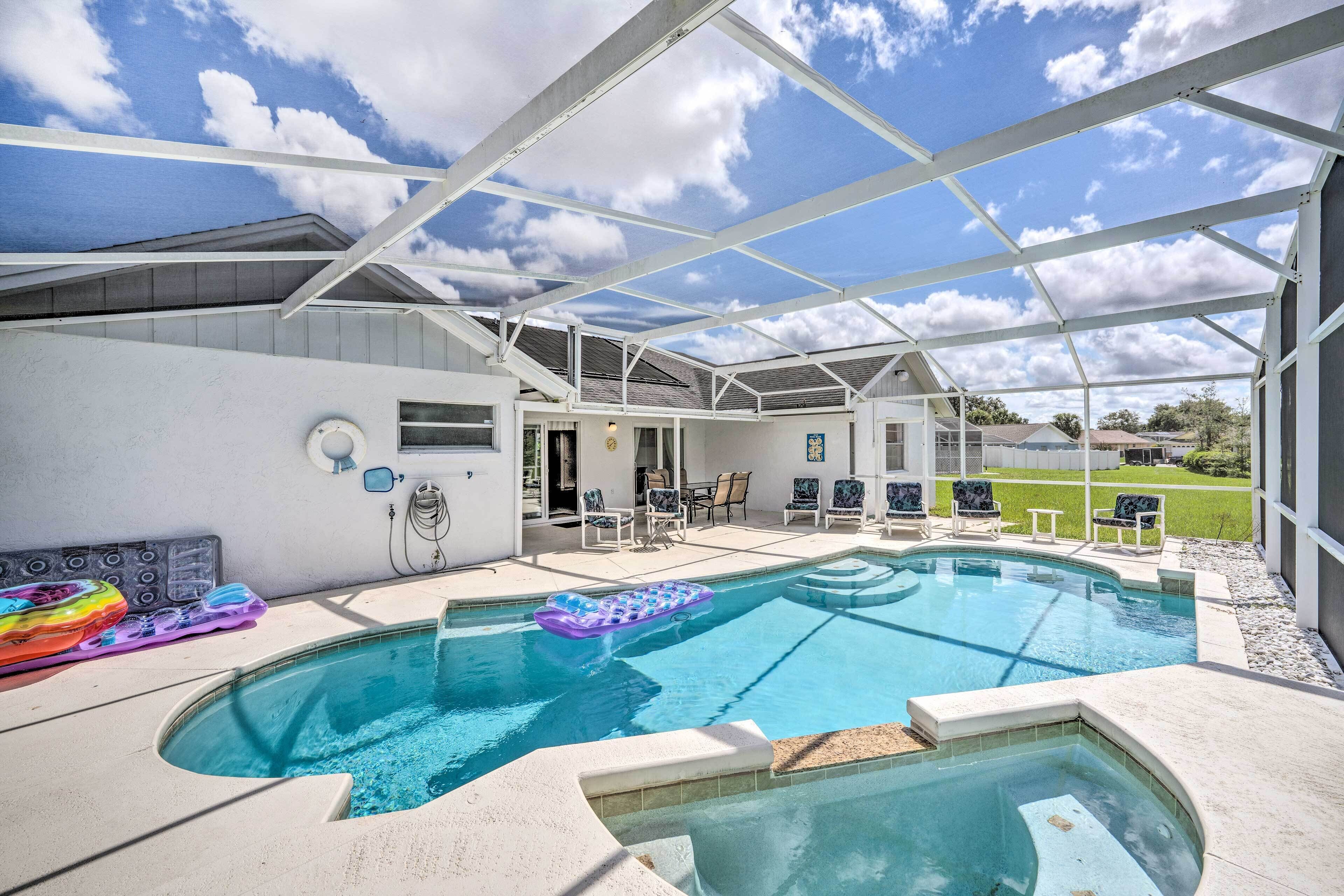 An outdoor swimming pool with a covered patio area, lounge chairs, and a view of the surrounding landscape.