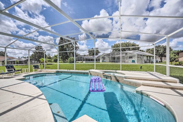 Una piscina techada con una colchoneta flotante, rodeada por una pérgola blanca y un césped.