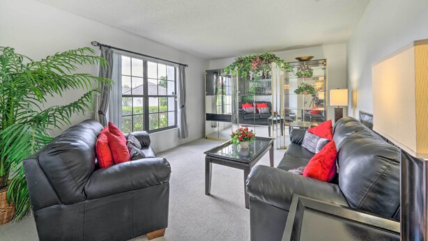 A modern living room with two black leather sofas, a glass coffee table, and a large potted plant. - Pool + Game Room, 5 Mi to Disney: Kissimmee Home! (Kissimmee)