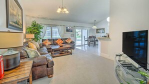 A spacious living room with a leather sofa, a coffee table, and a TV on a glass stand. There is a dining area with a table and chairs, and a large window providing natural light. - Pool + Game Room, 5 Mi to Disney: Kissimmee Home! (Kissimmee)