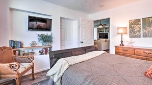Un dormitorio con cama, una silla, televisión, estantería y puerta que da a un baño.