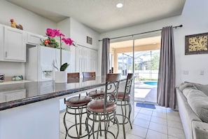 A modern kitchen with white cabinets, a central island with bar stools, and a view of the outdoor swimming pool. - Kissimmee Home w/ Pool < 9 Mi to Disney World! (Kissimmee)
