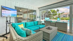 Ein großzügiger Wohnbereich mit einem großen, türkisfarbenen Sofa, Korbmöbeln, einem Flachbildfernseher und Blick auf einen Pool und Sitzgelegenheiten im Freien.