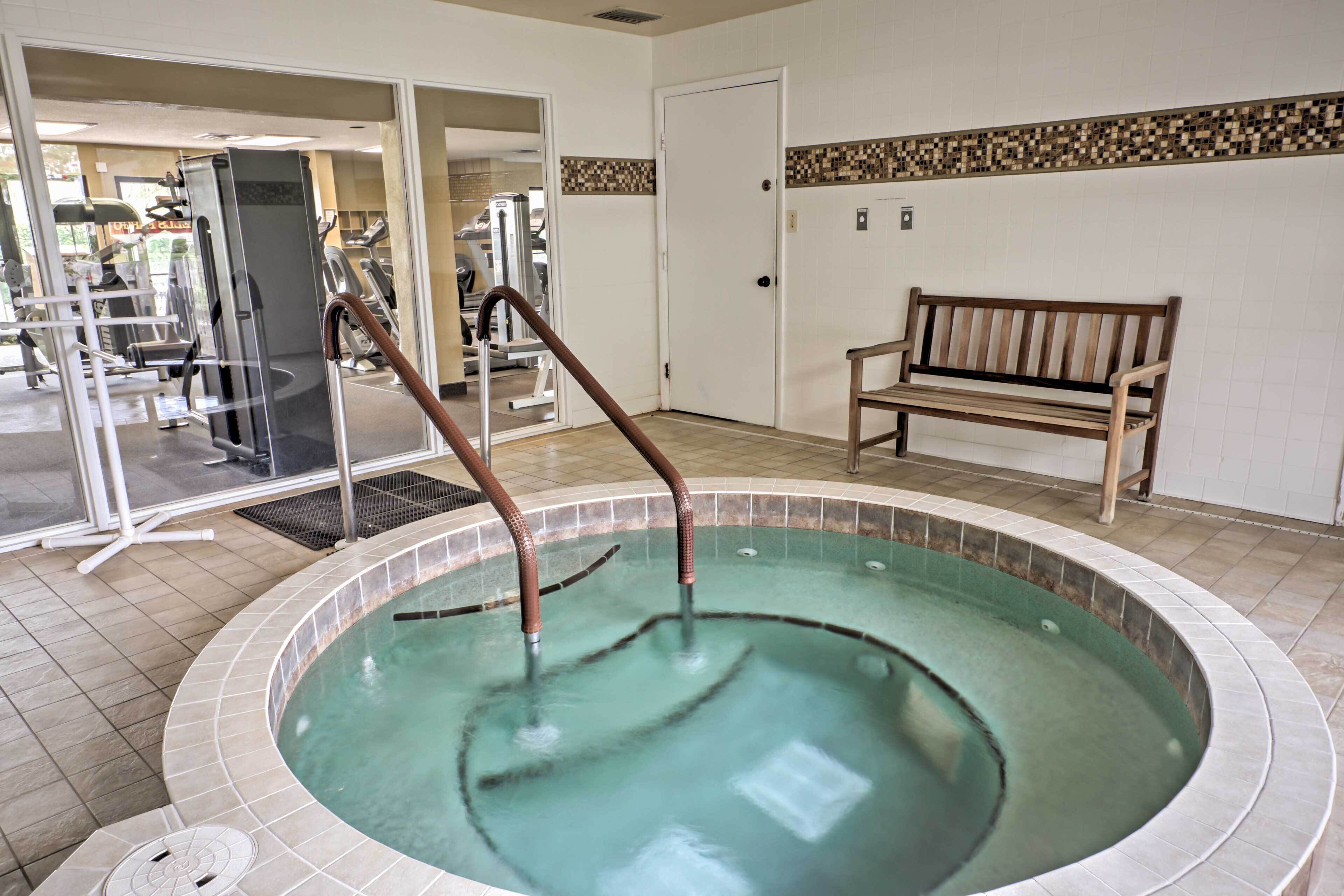 A hot tub with a wooden bench, a door, and exercise equipment in the background.