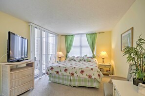 A bedroom with a bed, television, bedside tables, lamps, a desk, and a potted plant. - Beachfront Sarasota Resort Condo: Siesta Key View! (Siesta Key)