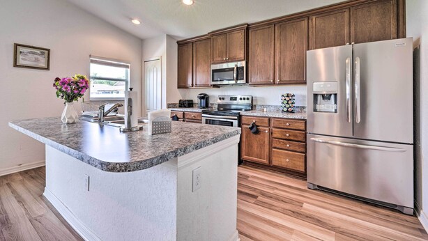 A modern kitchen with a granite countertop island, stainless steel appliances, wooden cabinets, and a view of the outdoors. - Bright Cypress Gardens Home Near Legoland! (Winter Haven)
