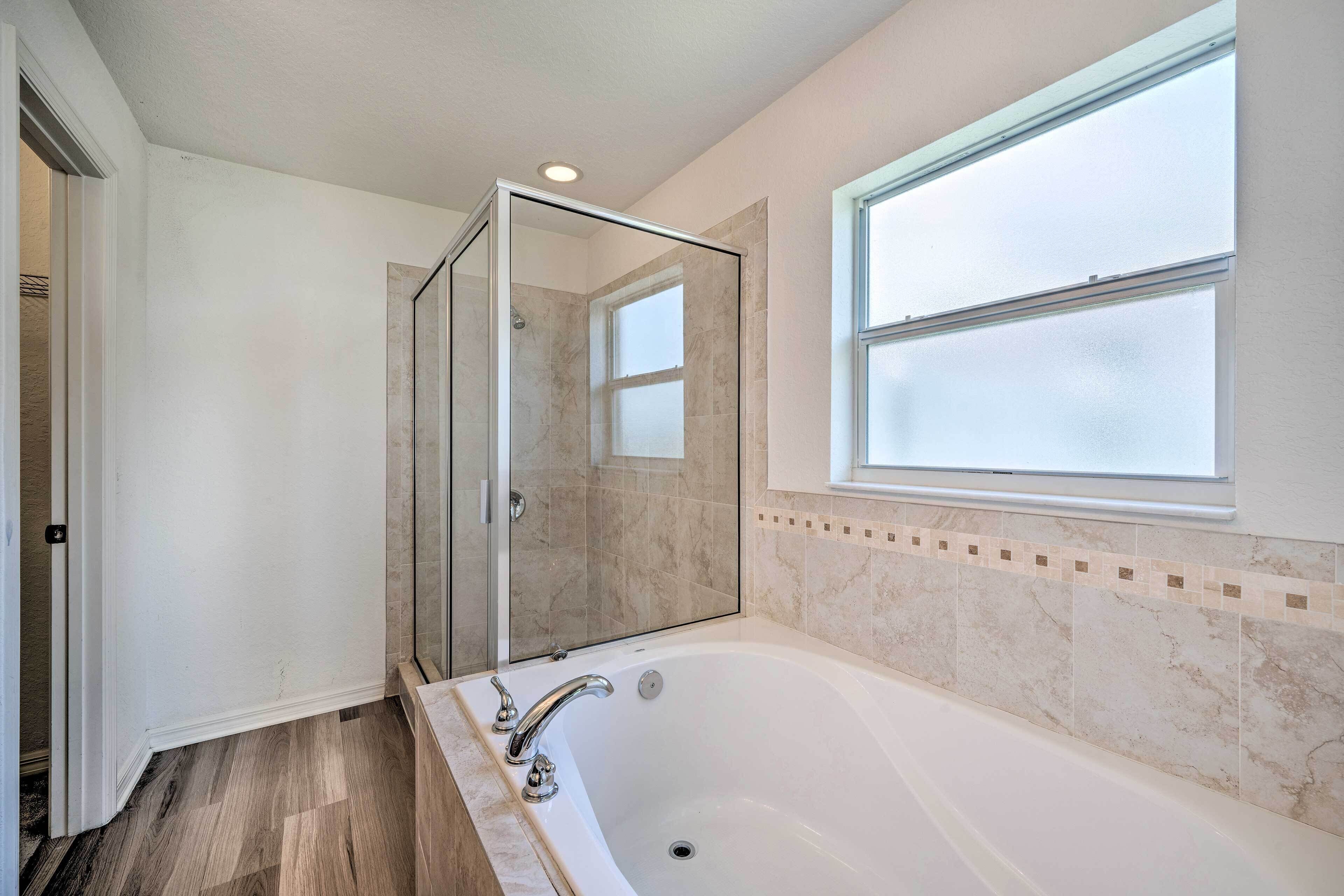 Un baño con ducha envuelta en vidrio, una bañera grande y un ventanal que proporciona luz natural.