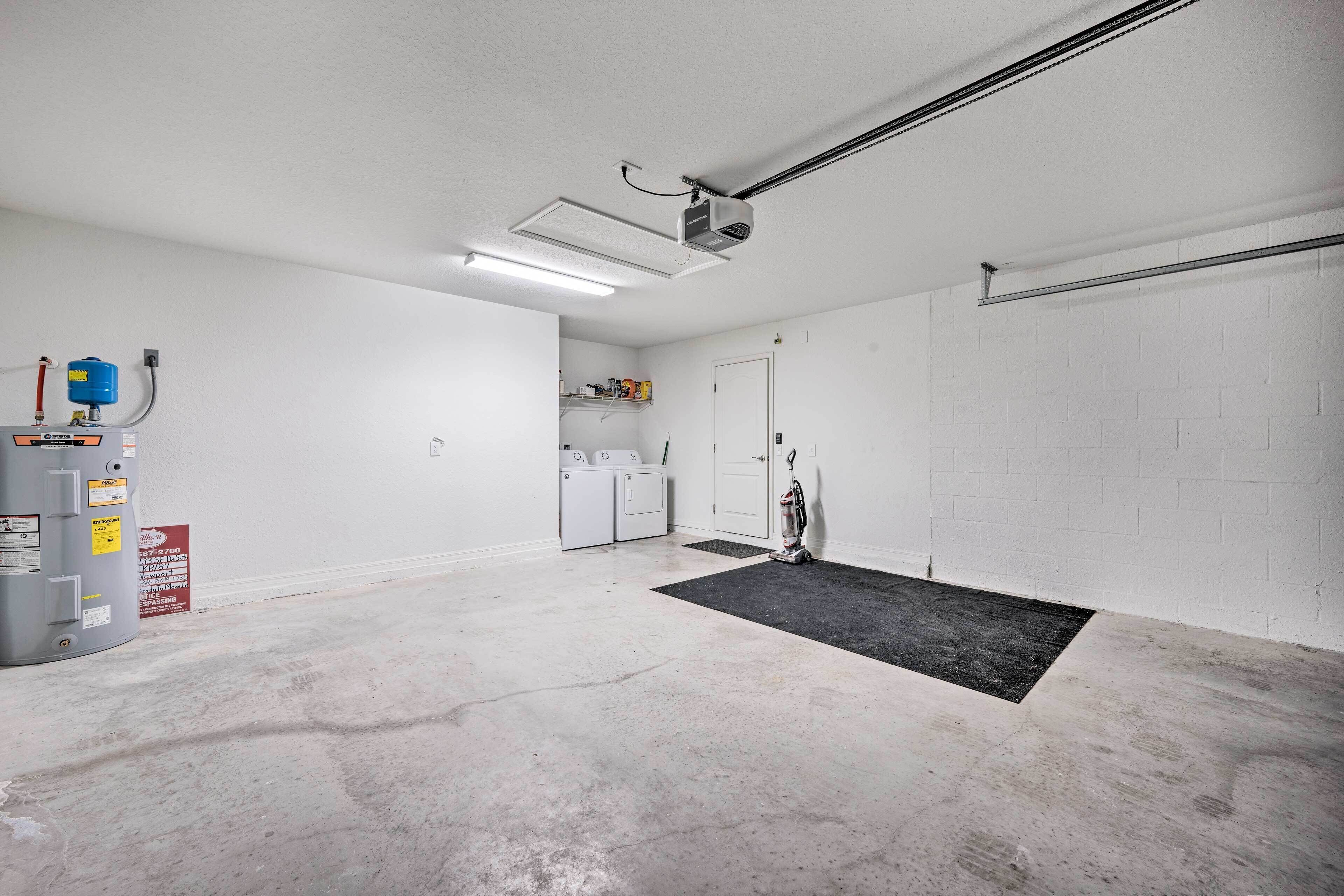 A garage with a concrete floor, a ceiling-mounted projector, a washing machine, and a vacuum cleaner.