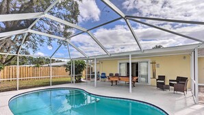 A covered outdoor swimming pool with a patio area, including chairs and a table.