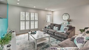 A living room with a white coffee table, grey sofa, and a large window with blinds.