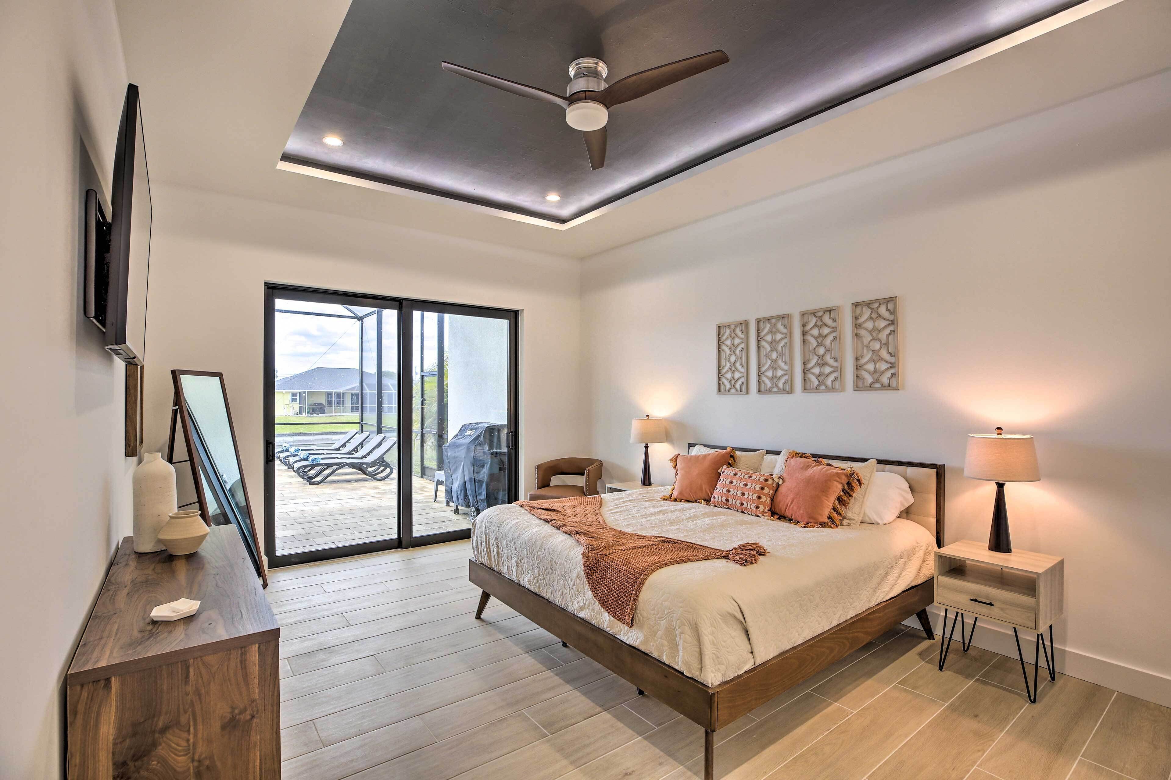 A bedroom with a bed, bedside tables, a ceiling fan, and a view to an outdoor area.
