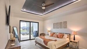 Ein Schlafzimmer mit Bett, Nachttischen, Deckenventilator und Blick ins Freie.