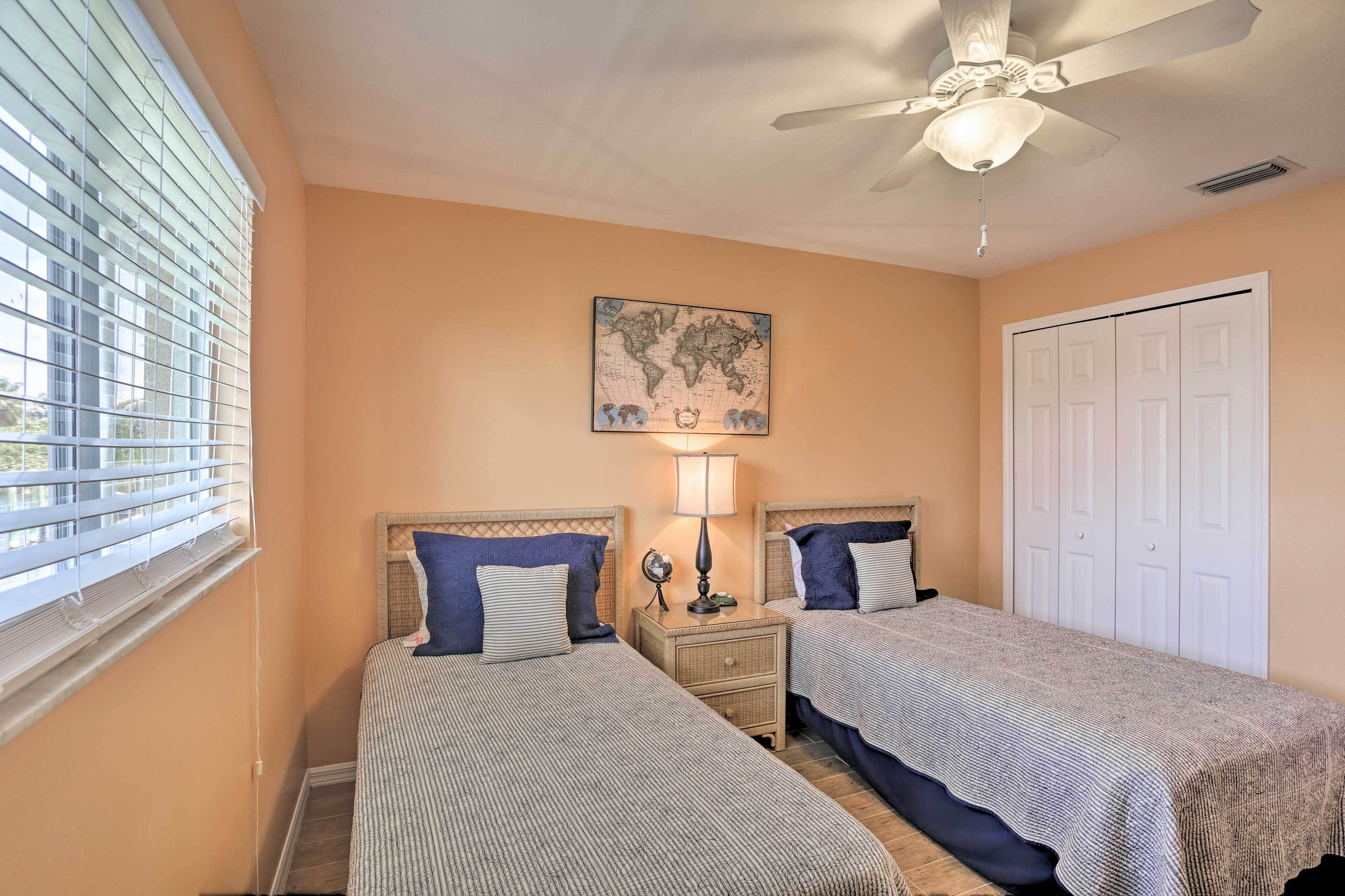 A bedroom with two beds, a ceiling fan, a world map artwork, and a white door.