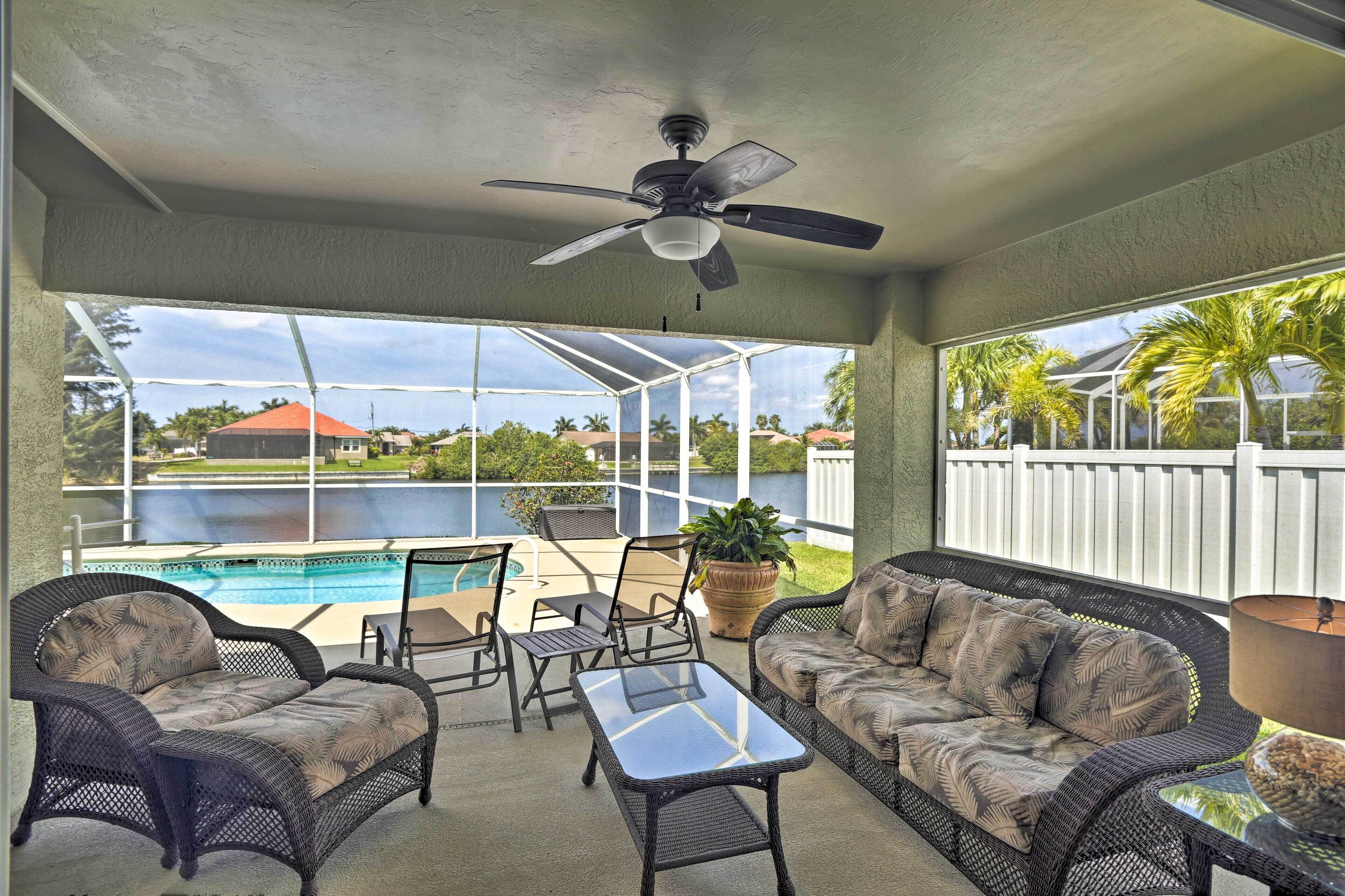 A covered patio with wicker furniture, a ceiling fan, and a view of a swimming pool.