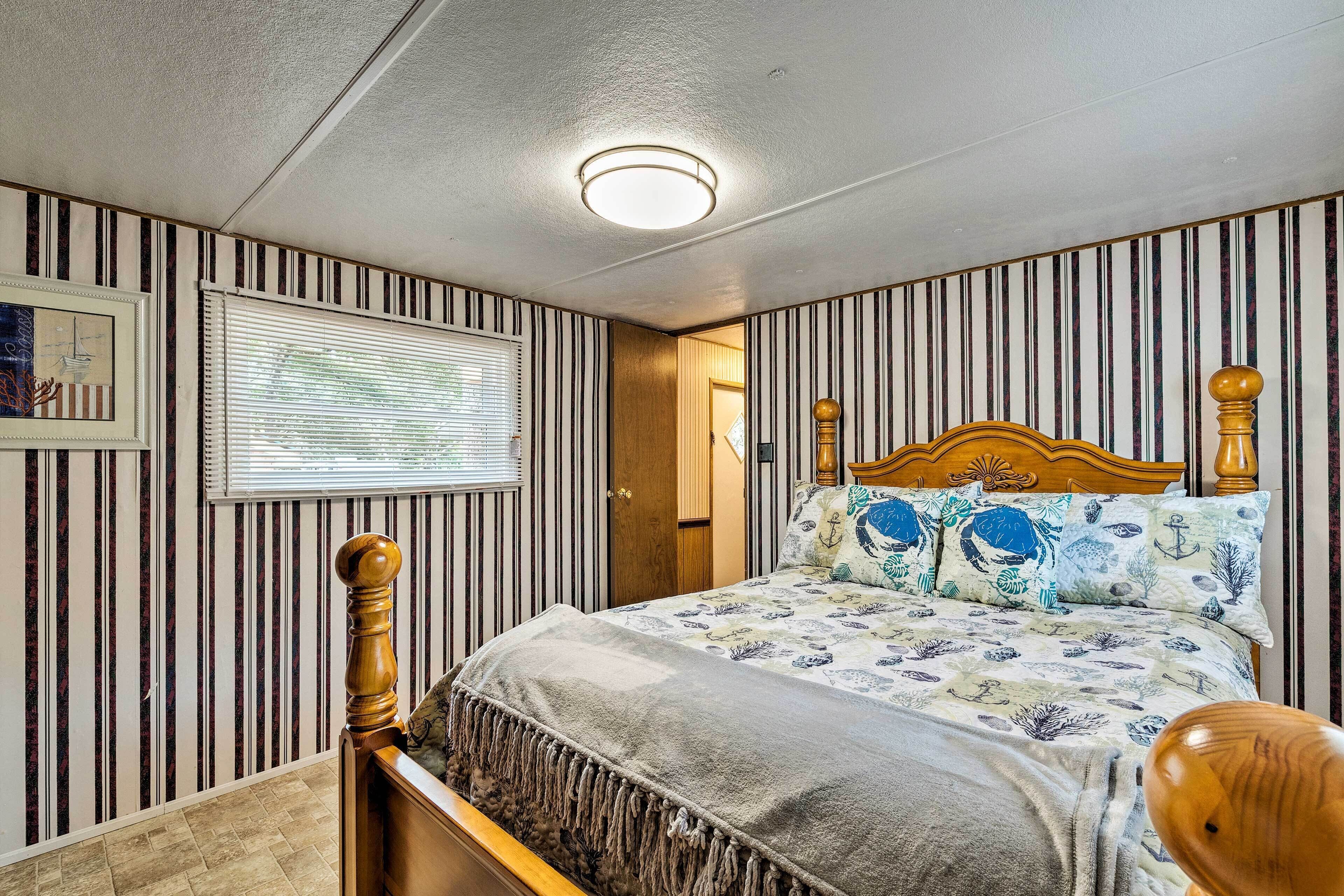A bedroom with striped wallpaper, a bed with a floral bedspread, a wooden headboard, and a window with blinds.