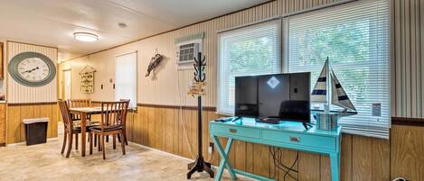 A room with a wooden paneled wall, a dining table with chairs, a television on a stand, and a clock on the wall.