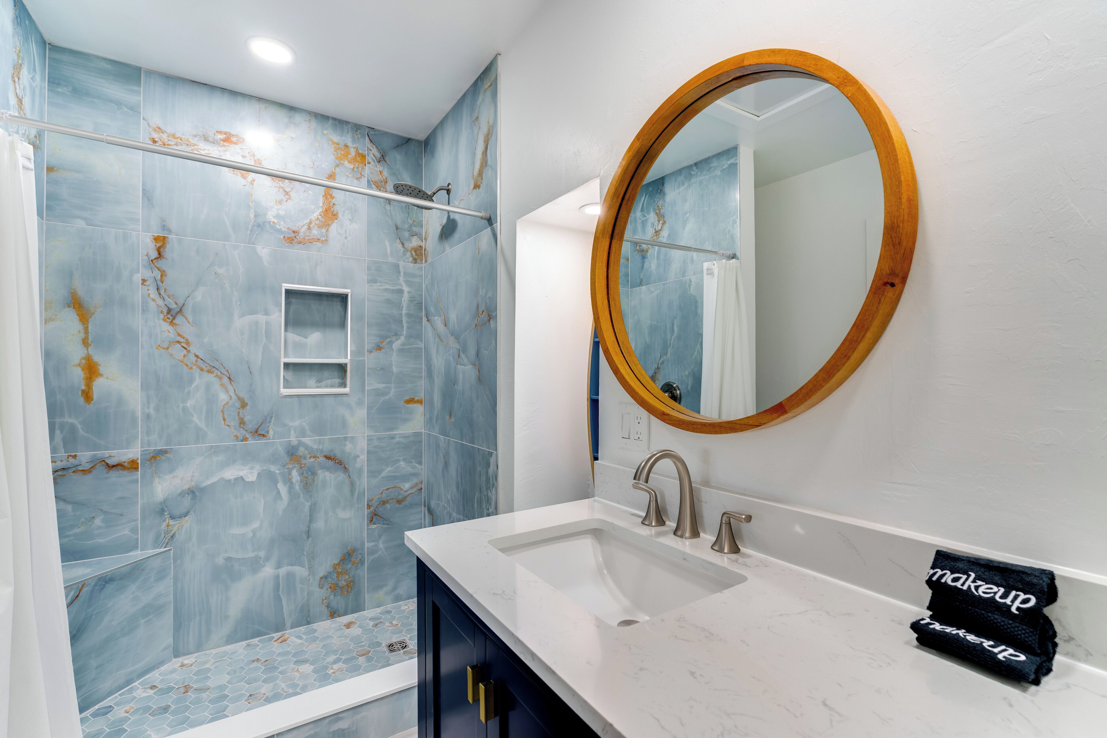 A bathroom with a white sink, a wooden-framed mirror, and blue marble tiles.