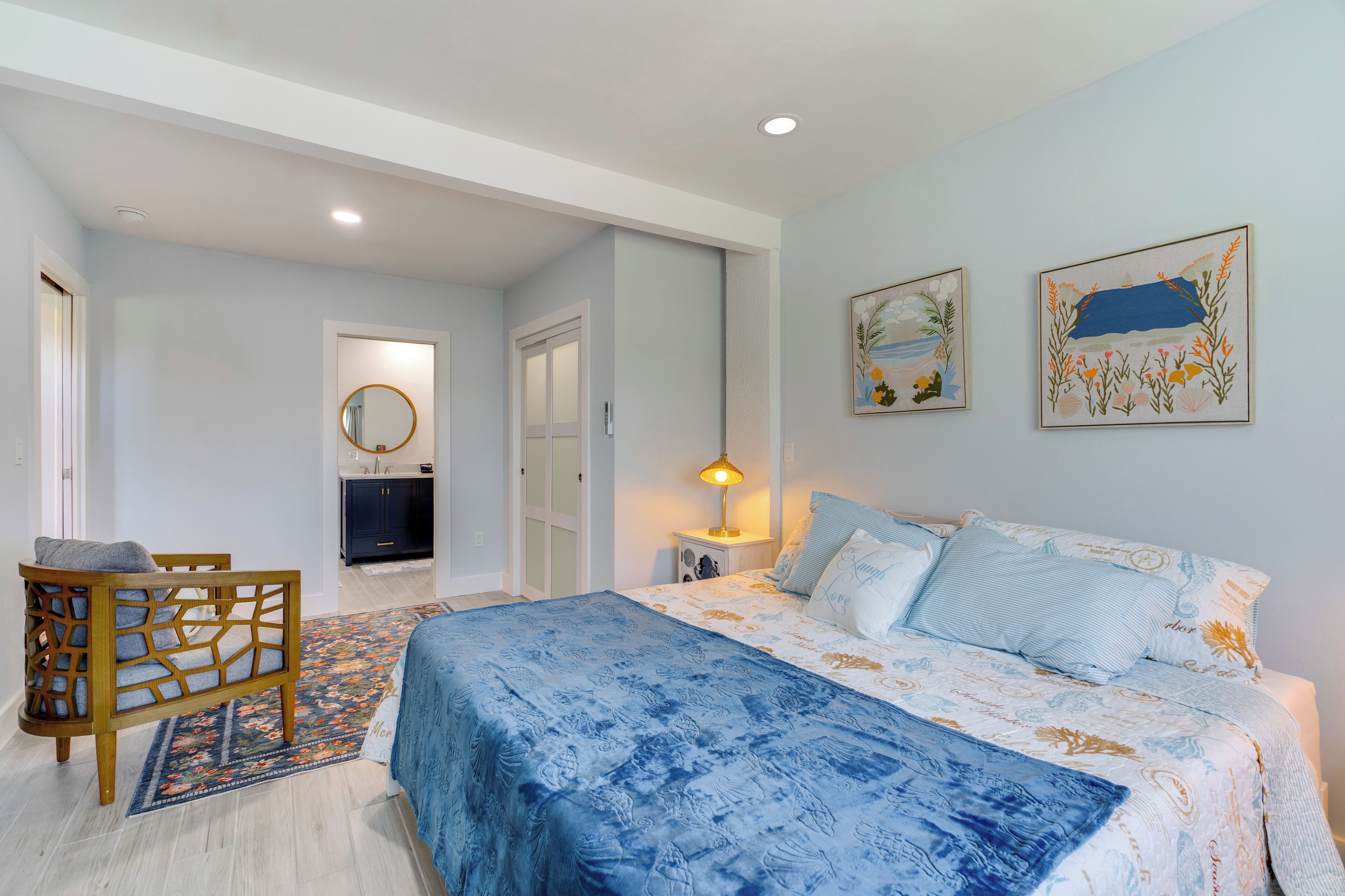 A bedroom with a bed, a chair, a nightstand, and two wall-mounted paintings.