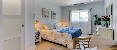 Ein Schlafzimmer mit einem Bett, Nachttischen, einem Sessel, einem Teppich und einem Fenster mit Vorhängen.