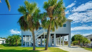 A two-story house with a covered porch, palm trees, and a clear blue sky. - Canalfront St James City Home w/ Unique View (Saint James City)