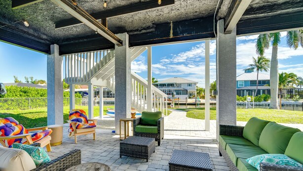 An outdoor patio area with wicker furniture, a green sofa, and a staircase leading to an upper level. - Canalfront St James City Home w/ Unique View (Saint James City)