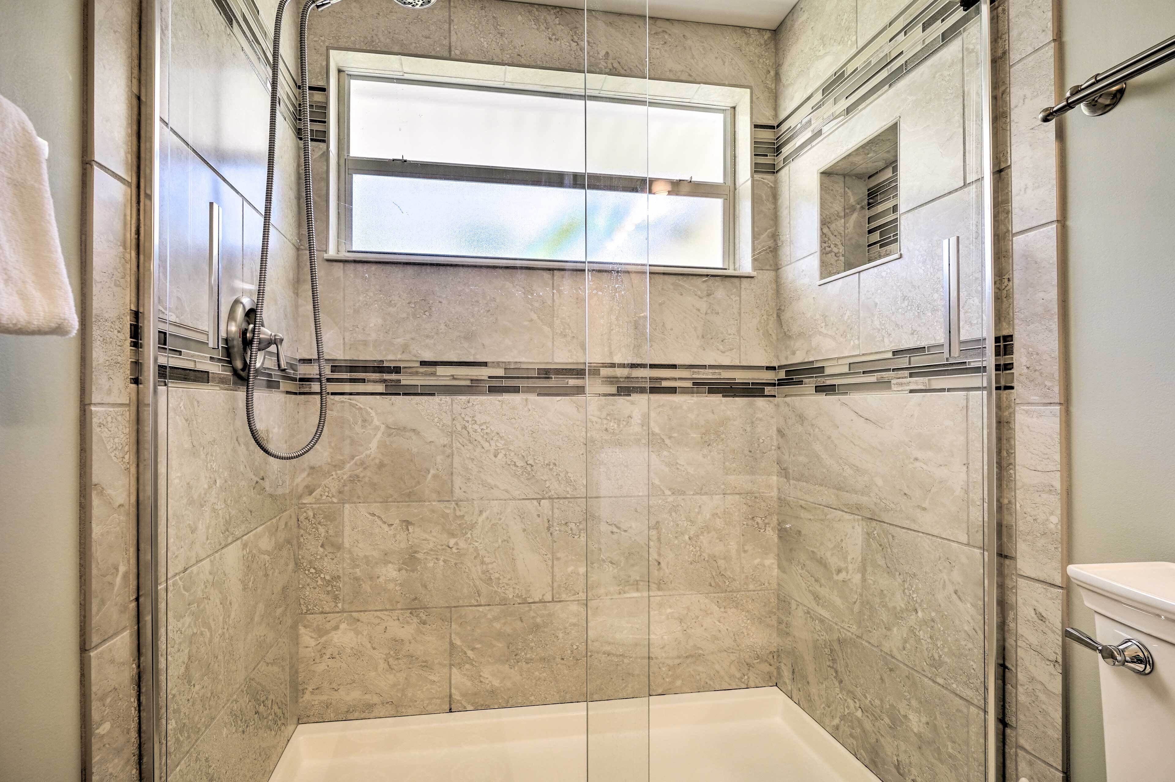 A modern bathroom with a glass-enclosed shower, a bathtub, and a window providing natural light.