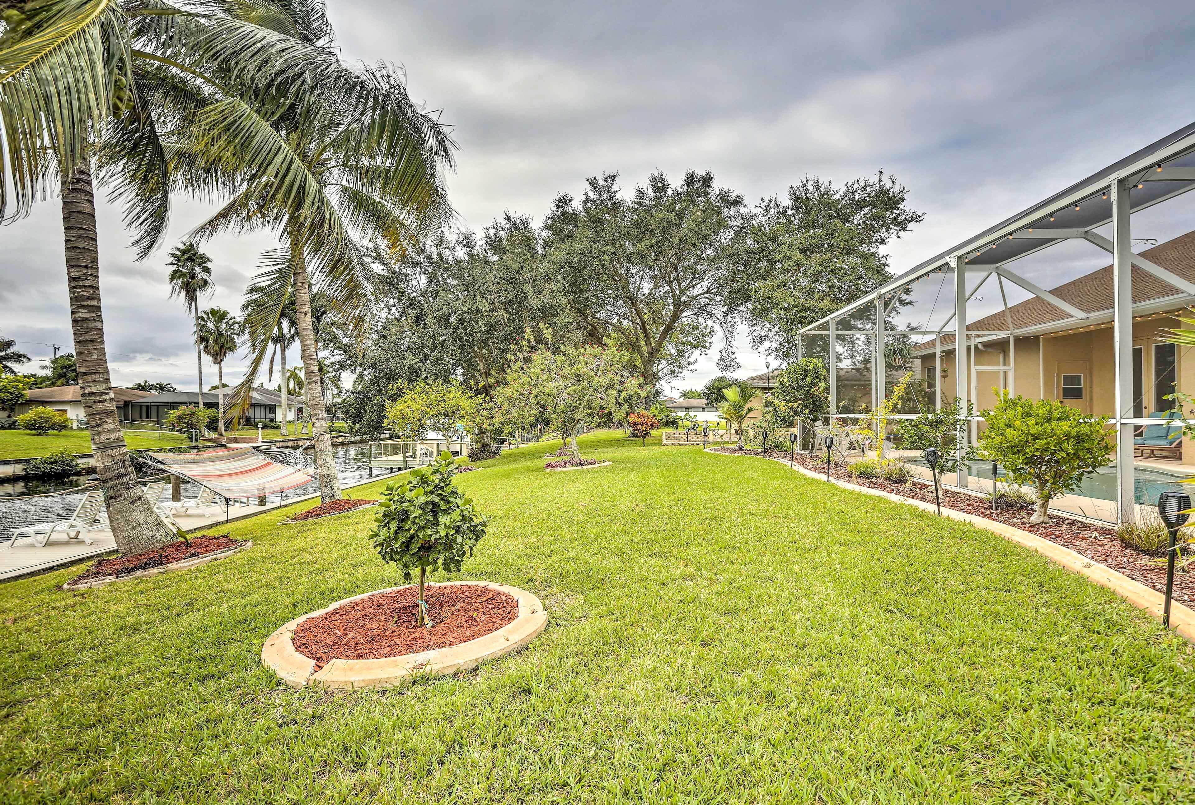 A well-maintained lawn with a circular flower bed, palm trees, and a covered patio area.