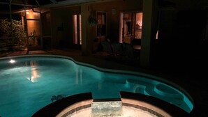 Ein Schwimmbad mit einem Whirlpool in der Mitte, umgeben von einem Haus mit Terrasse und Gartenmöbeln.