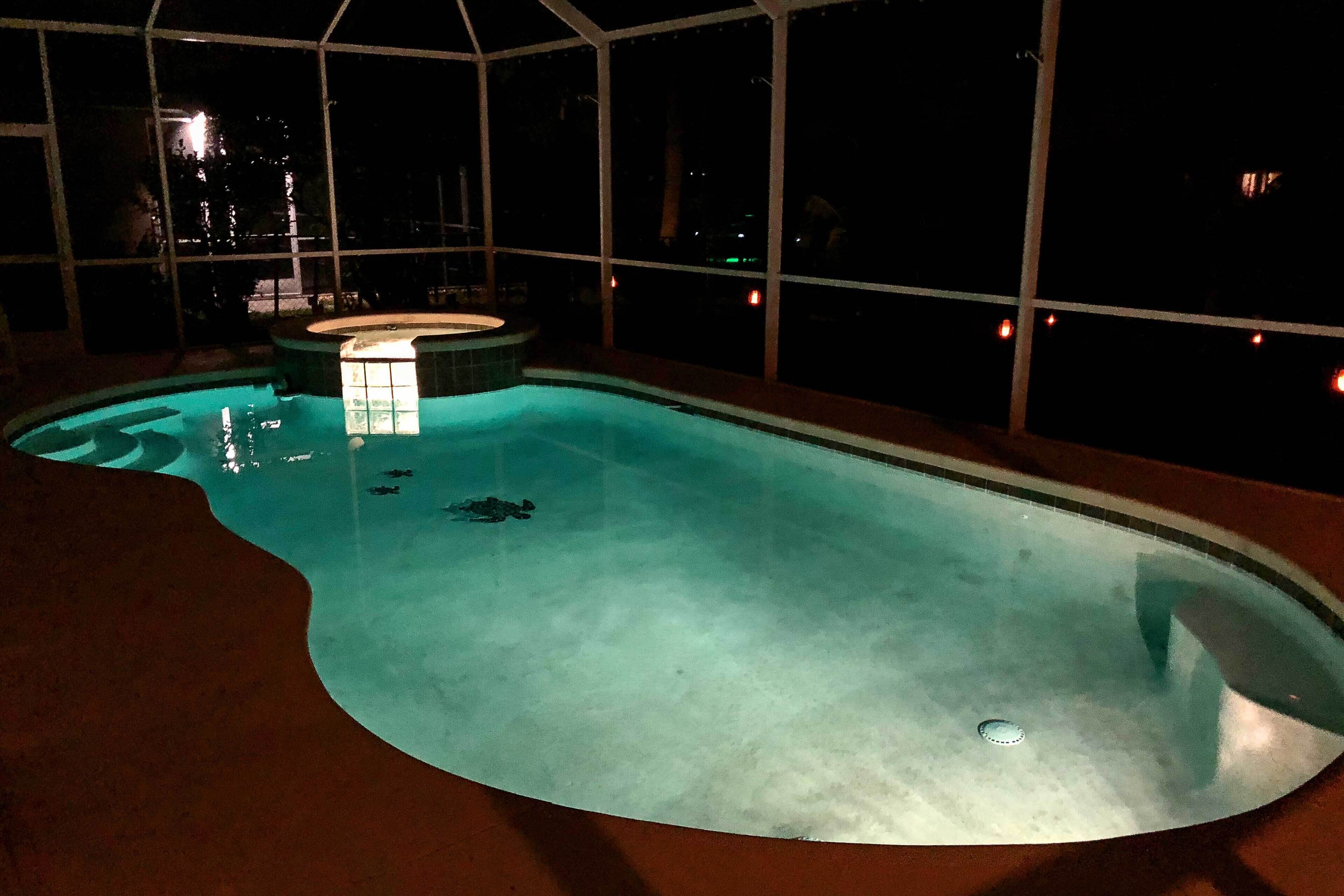 An indoor swimming pool with a hot tub, surrounded by a glass enclosure with a view of the night sky.