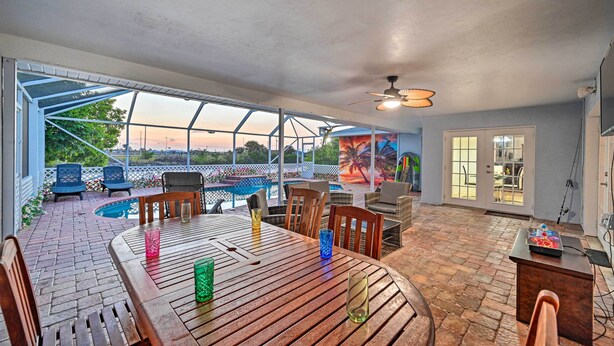 A covered patio area with a pool, wooden table and chairs, and a view of the sunset. - Canal-front Cape Coral Home w/ Patio & Grill! (Cape Coral)