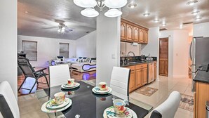 A dining area with a black table, white chairs, and a chandelier. There is a kitchen with wooden cabinets and a refrigerator. - Canal-front Cape Coral Home w/ Patio & Grill! (Cape Coral)