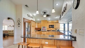 A modern kitchen with wooden cabinets, a central island with stools, and pendant lighting. - Private Dock: Canalfront Home in Cape Coral (Cape Coral)