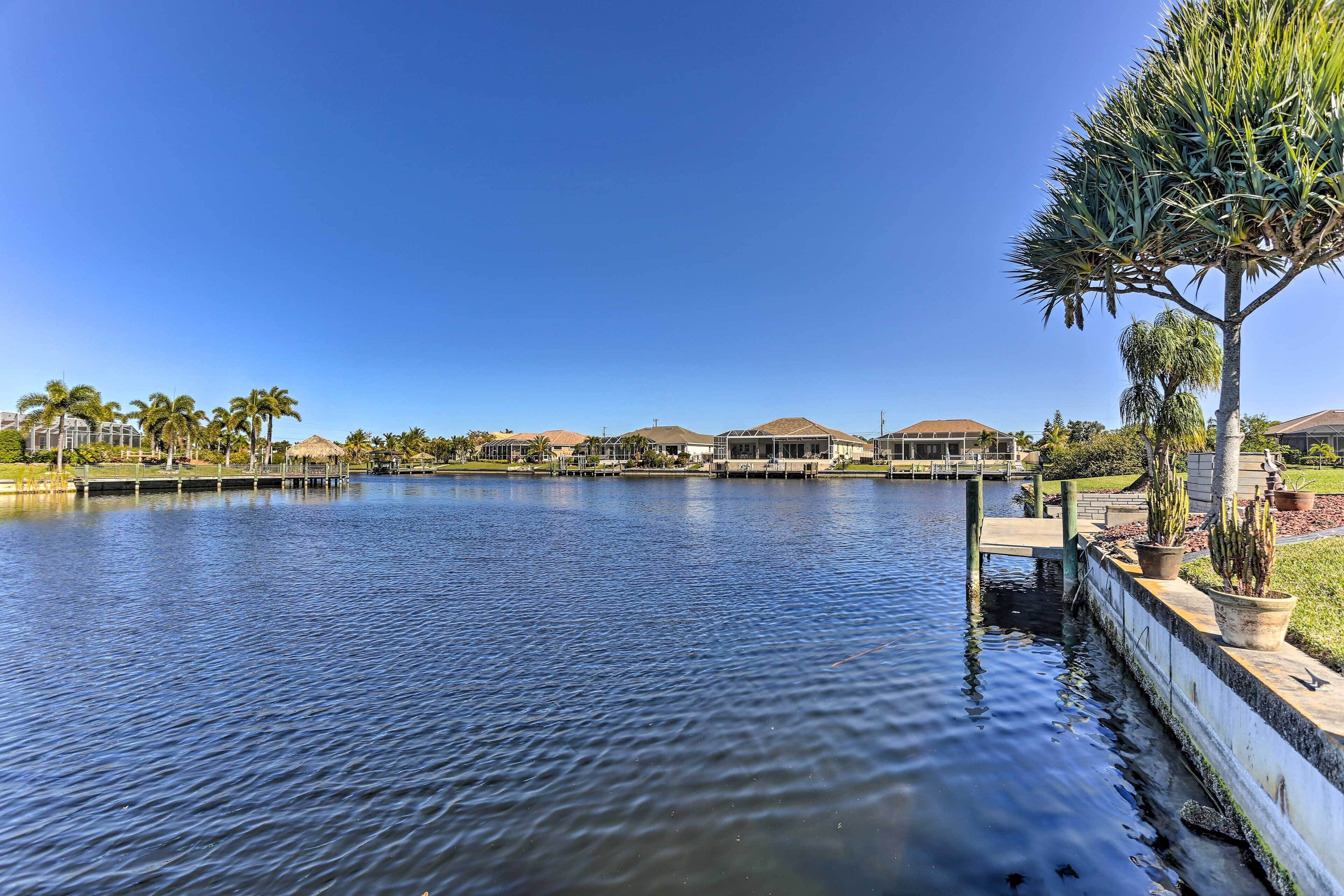 A calm lake with a dock, surrounded by palm trees and buildings with brown roofs.