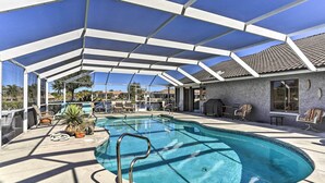 A covered outdoor swimming pool with a clear blue water, surrounded by lounge chairs and potted plants. - Private Dock: Canalfront Home in Cape Coral (Cape Coral)