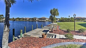 A waterfront property with a dock, a concrete walkway, and a grassy area with a statue. - Private Dock: Canalfront Home in Cape Coral (Cape Coral)