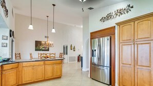 A spacious kitchen with wooden cabinets, a stainless steel refrigerator, pendant lights, and a dining area with chairs. - Private Dock: Canalfront Home in Cape Coral (Cape Coral)