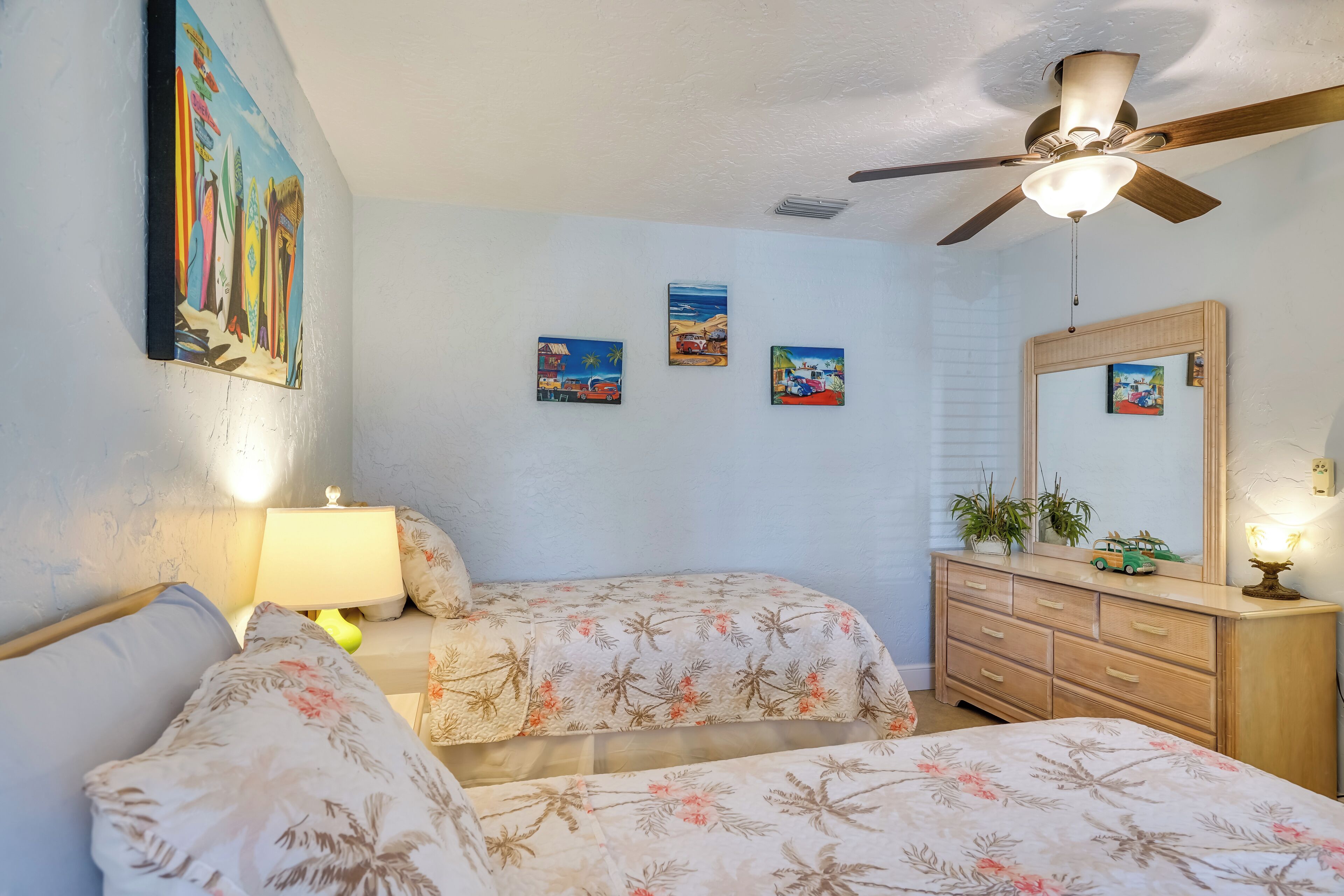 A bedroom with two beds, a ceiling fan, a dresser, and wall art.