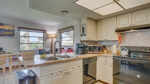 A modern kitchen with white cabinets, a stainless steel stove, a coffee maker, and a sink.