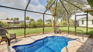 An outdoor swimming pool with a covered patio area, a chair, and a safety railing. - Canal-front Retreat w/ Heated Pool & Hot Tub! (Port Charlotte)