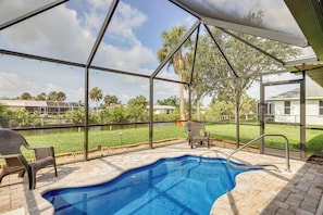 An outdoor swimming pool with a covered patio area, a chair, and a safety railing.