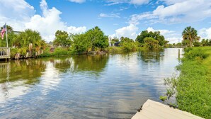 A calm river with a dock, surrounded by lush greenery and a clear sky. - Canal-front Retreat w/ Heated Pool & Hot Tub! (Port Charlotte)