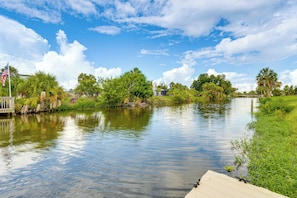 A calm river with a dock, surrounded by lush greenery and a clear sky.
