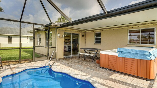 A backyard with a swimming pool, a hot tub, and a patio area with a table and chairs. - Canal-front Retreat w/ Heated Pool & Hot Tub! (Port Charlotte)