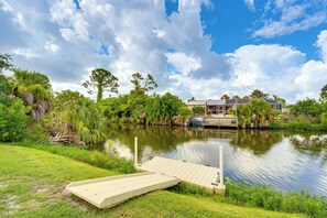 A lakeside property with a dock, lush greenery, and a house in the background.
