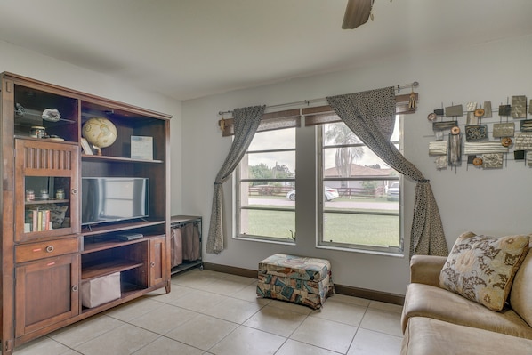 Quarto com móvel de entretenimento em madeira, um sofá, uma janela com cortinas e parede decorada com diversos objetos.