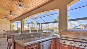 A kitchen with a built-in grill, wooden cabinets, and a large window overlooking a residential area. - 'casa Getaway' Cape Coral Home w/ Lanai & Pool! (Cape Coral)