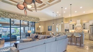 A spacious living area with a large sectional sofa, a ceiling fan, and a kitchen with bar stools and modern appliances. - 'casa Getaway' Cape Coral Home w/ Lanai & Pool! (Cape Coral)