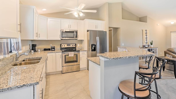 A modern kitchen with granite countertops, stainless steel appliances, and a central island with bar stools. - Central Cape Coral House w/ Private Screened Pool! (Cape Coral)